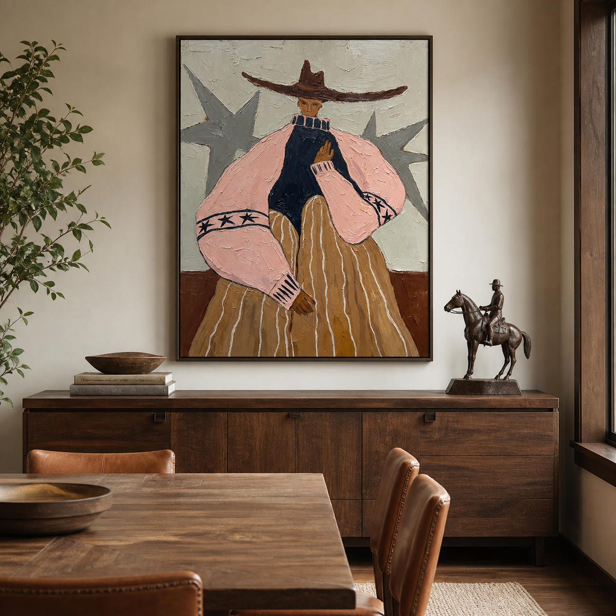Western woman wall art with a wide brown hat, pink sleeves and ochre skirt displayed above a leather sofa.