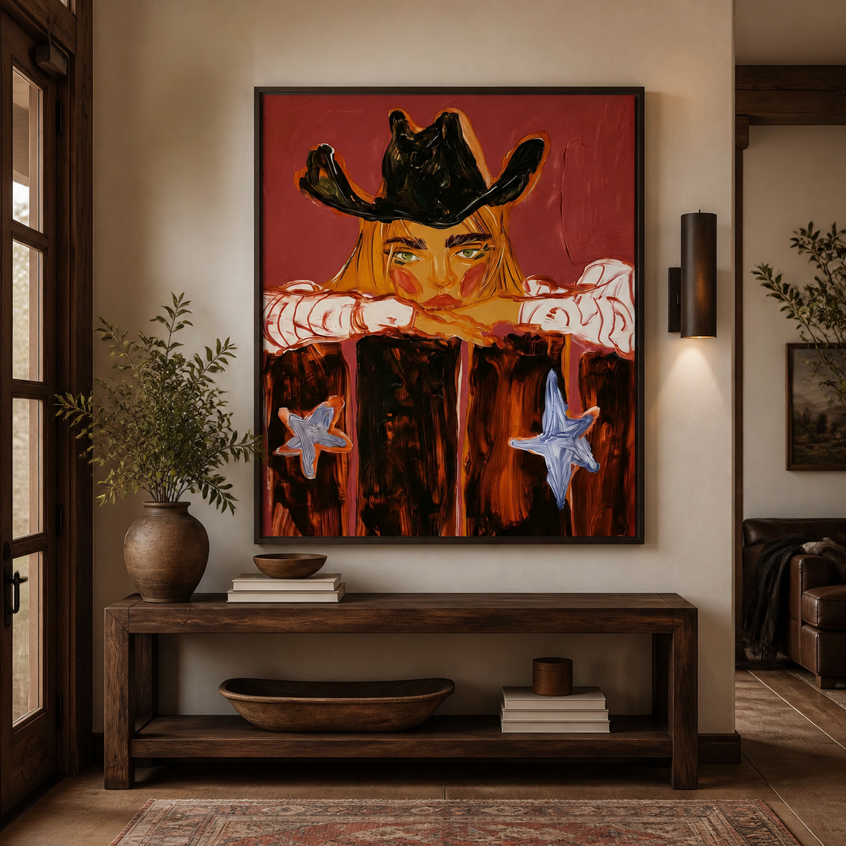 Cowgirl portrait wall art showing a blonde woman resting beneath a black cowboy hat on a red background above an entryway console.