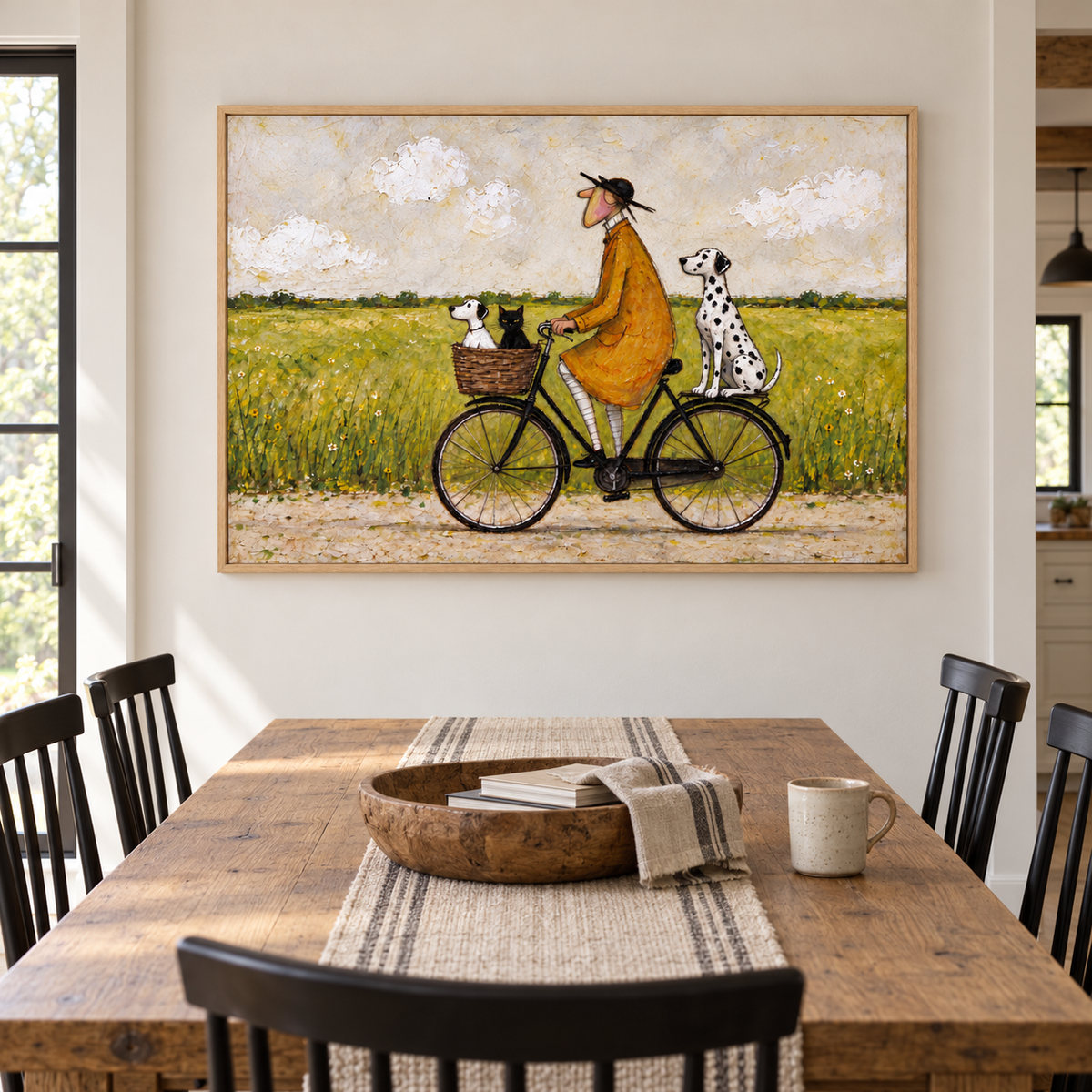 A man in an ochre coat riding a black bicycle with a small white dog and black cat in the front basket and a Dalmatian sitting over the rear wheel beside a green meadow, shown in room setting 2.