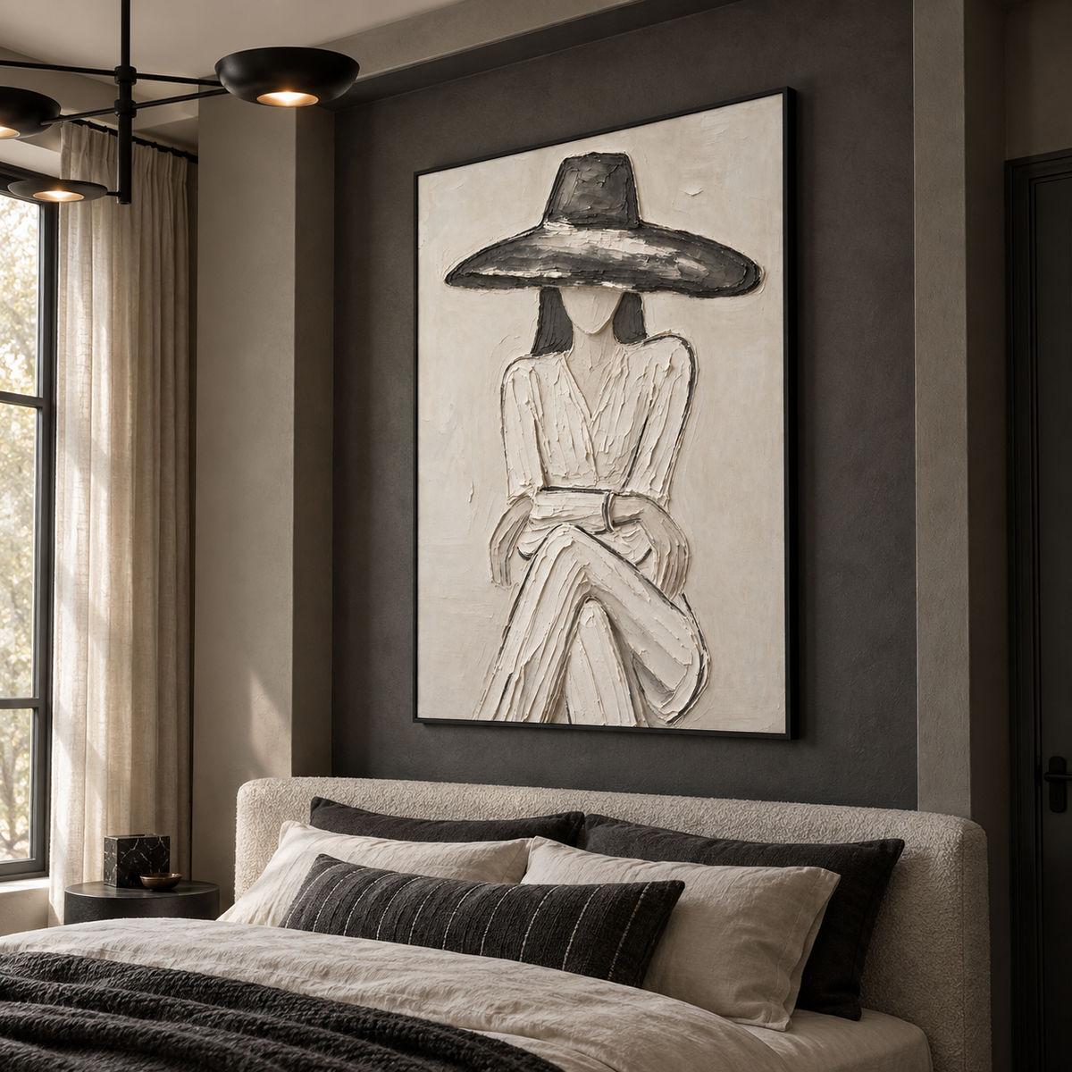A seated woman in a pale dress and broad charcoal hat with folded hands against an off-white background, shown from an angle in the room.