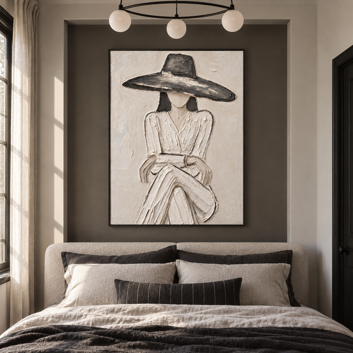 A seated woman in a pale dress and broad charcoal hat with folded hands against an off-white background, shown in a transitional bedroom.