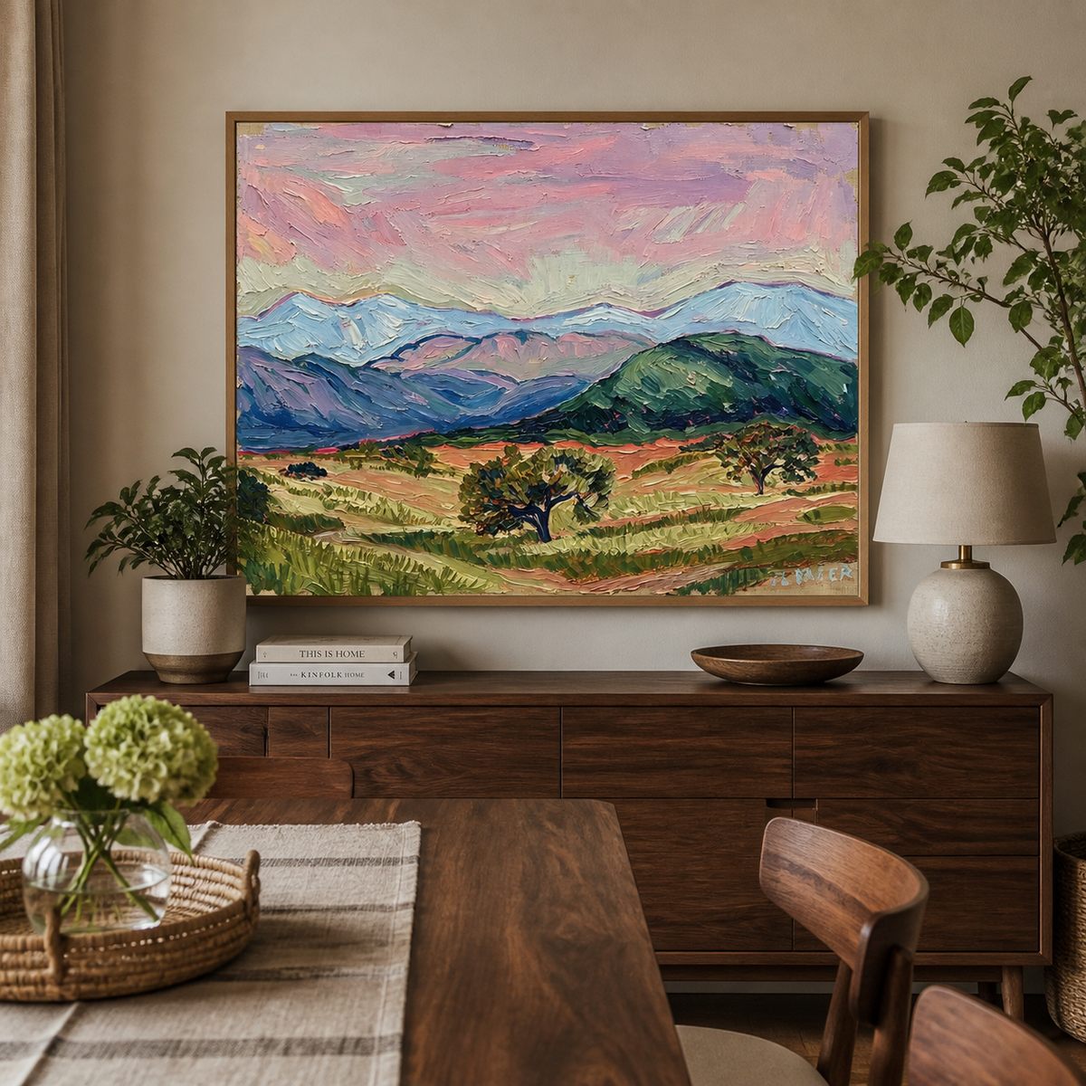 Colorful mountain landscape wall art with a pink sky, blue peaks and green valley displayed above a neutral sofa.