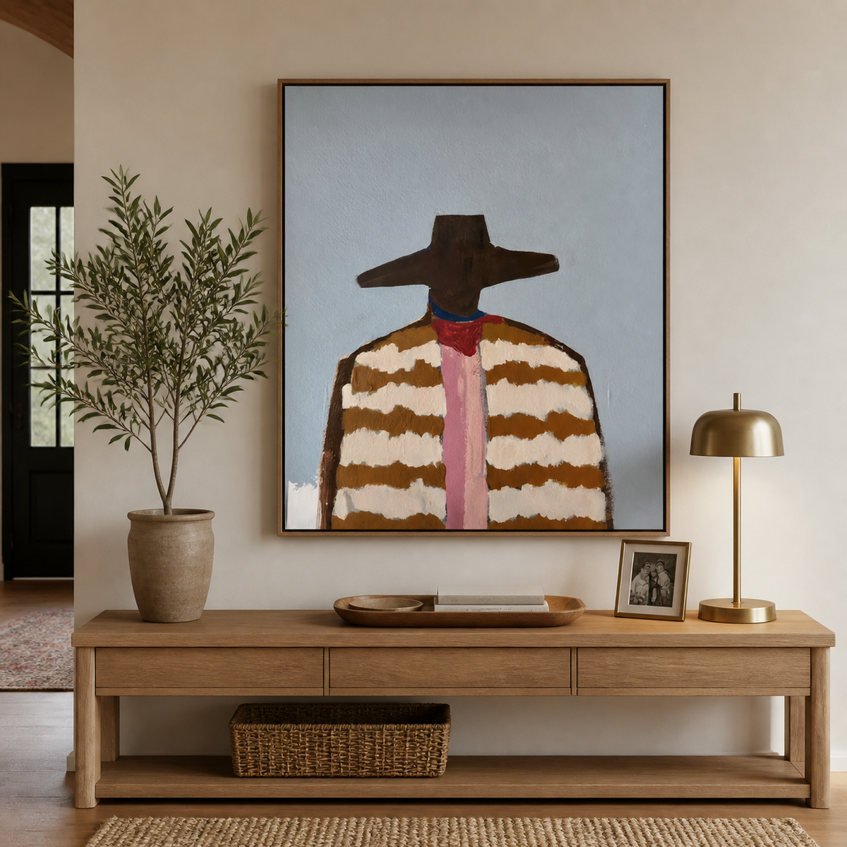 Western cowboy portrait with a wide brown hat, striped jacket and pink necktie displayed above a neutral sofa.