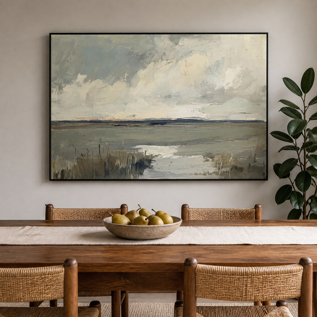 Neutral coastal wall art with a tidal marsh, cloudy sky and gray-blue textured shoreline displayed above a wooden dining table.