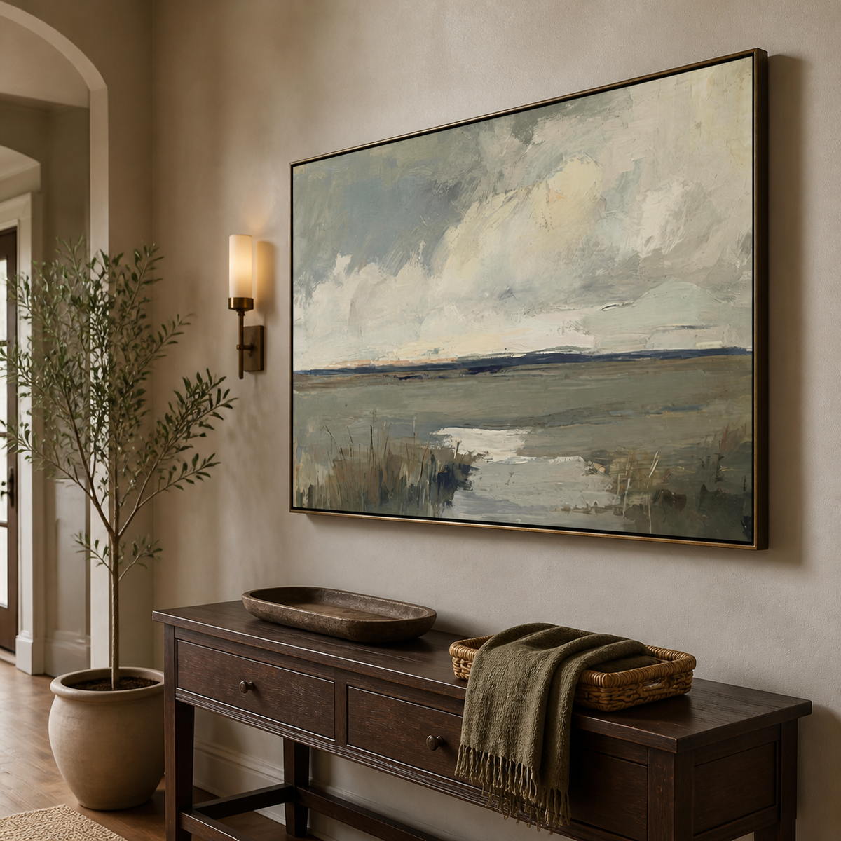 Neutral coastal wall art with a tidal marsh, cloudy sky and gray-blue textured shoreline displayed above a wooden dining table.
