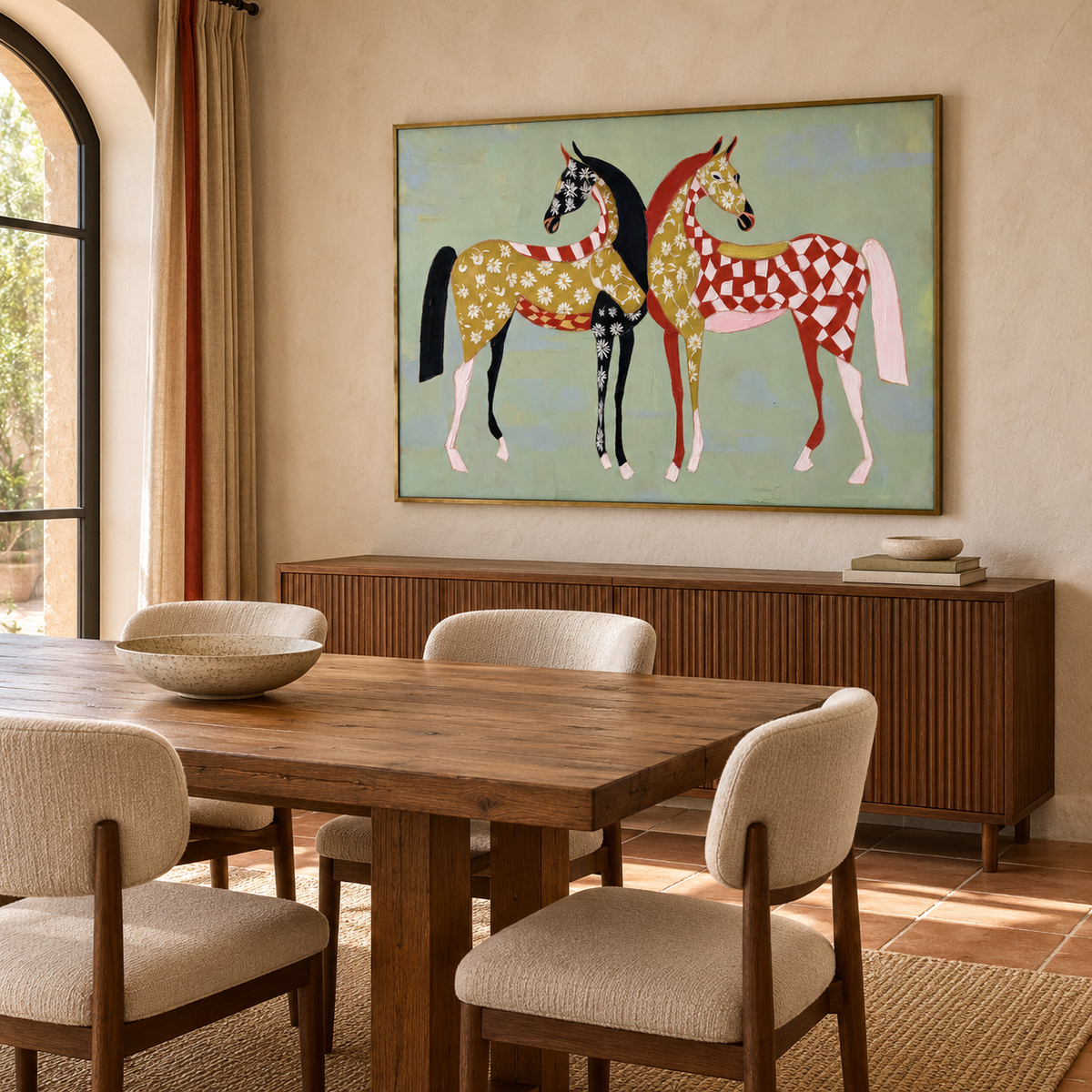 Two stylized horses stand close together against a pale blue field. One is decorated with small cream flowers and dark patches; the other carries a red-and-cream checker pattern with gold accents., shown from an angle in a dining room.