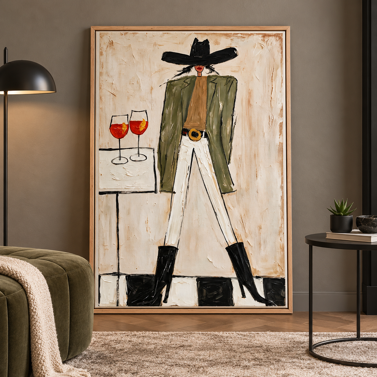 A woman in a wide black cowboy hat, olive-green jacket, white pants and black boots standing beside a small table with two orange-red drinks in stemmed glasses, shown in room setting 3.